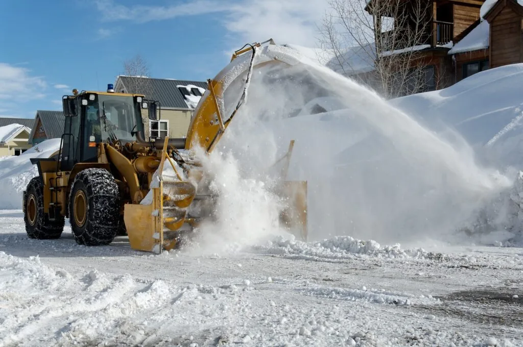 snow blower on the street in front of some houses