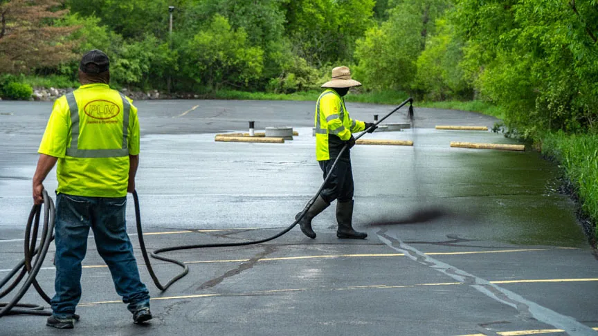 two plm paving employees applying sealcoat to a parking lot