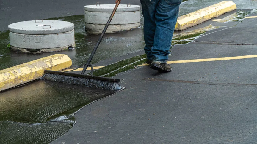 person applying sealcoat to pavement