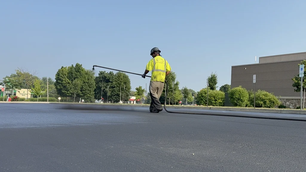 PLM employee applying sealcoat to asphalt surface