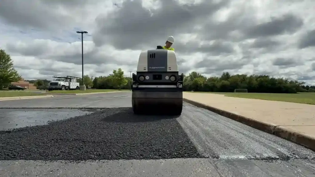PLM worker performing asphalt patching over a pothole in a local parking lot