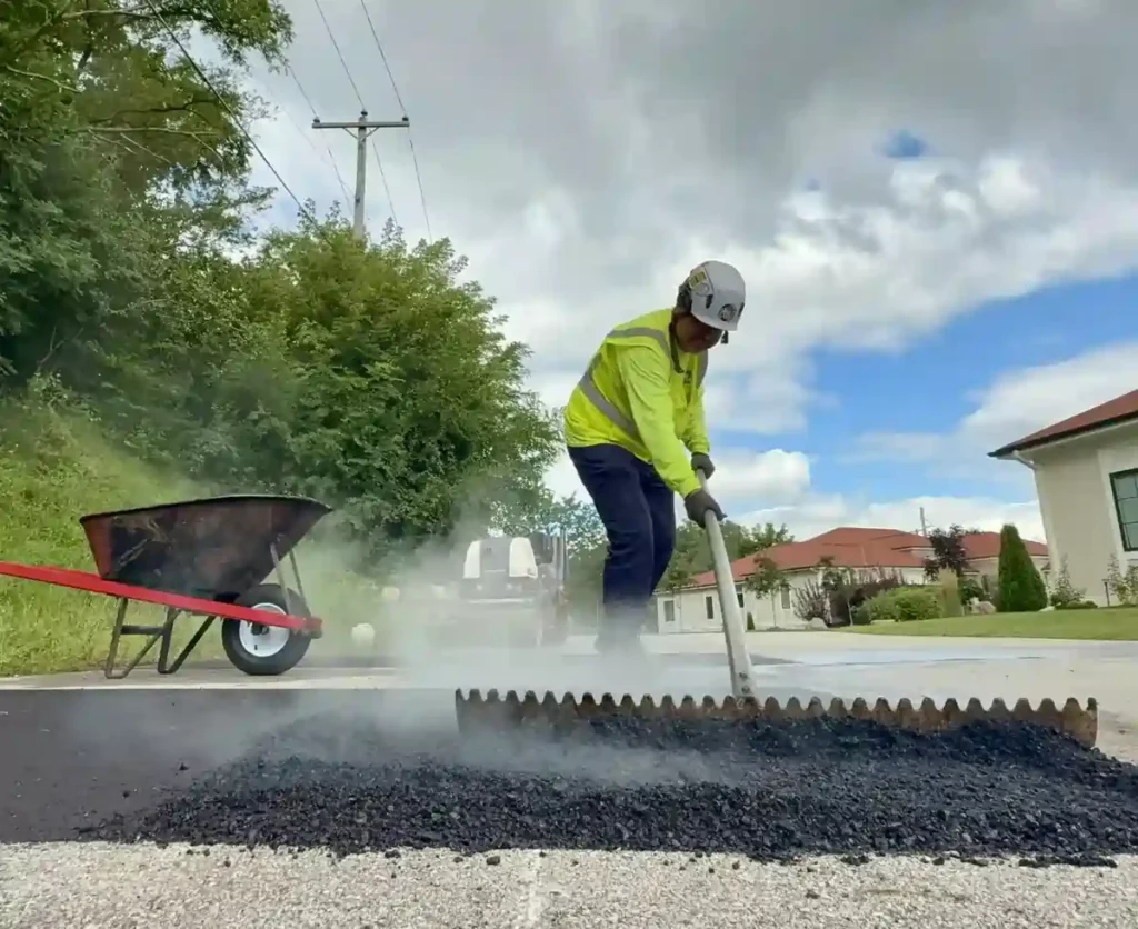 PLM worker raking hot asphalt for a repair project