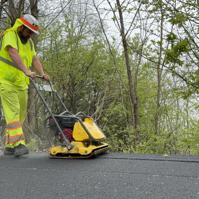 PLM employee compacting the fresh asphalt with a wacker at Juneau Park.