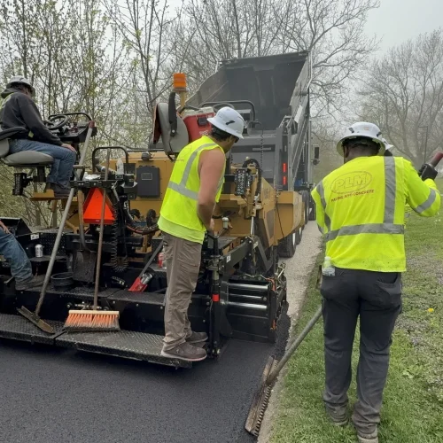 PLM employees laying down fresh asphalt while maintaining clean edges of the walking path at Juneau Park.